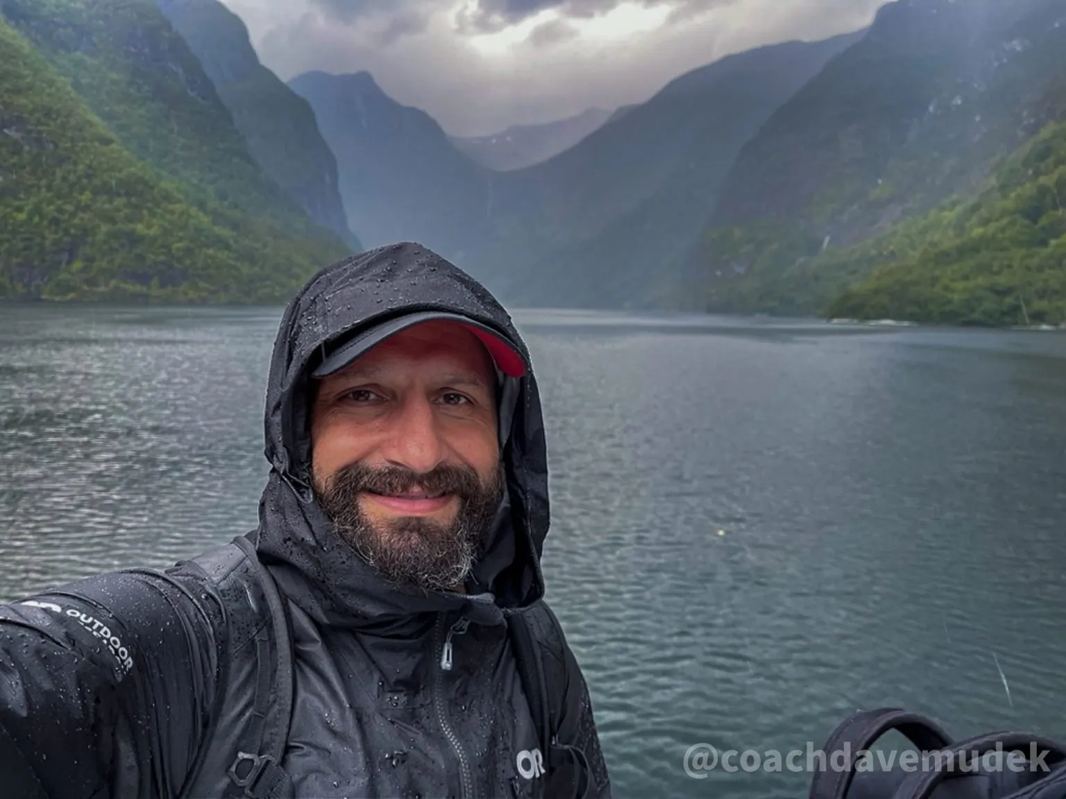 Dave Mudek in rain gear on the water, steep green mountains behind